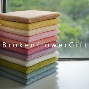 May include: A stack of ten colorful, fluffy cushions in various shades of brown, yellow, pink, purple, white, green, and blue. The cushions are arranged in a stack, with the brown cushion on top and the blue cushion on the bottom.