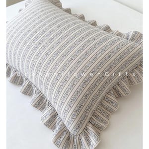 Könnte beinhalten: Rechteckiges Kissen mit einem gestreiften Muster in Creme und Hellblau, verziert mit einem floralen Design. Das Kissen hat einen gerüschten Rand und den Text "B Flower Gifts".