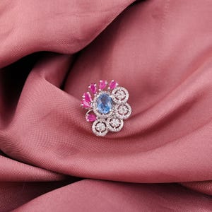 May include: A silver ring with a blue oval gemstone surrounded by smaller diamonds and pink gemstones.