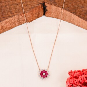 May include: A delicate rose gold necklace with a flower pendant. The flower is made of small red and white gemstones.