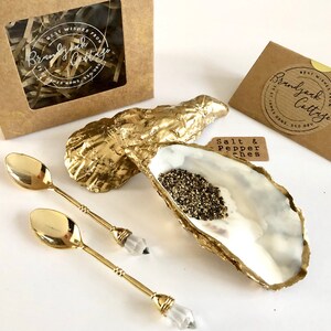 Op de afbeelding: Gouden oesterschelp zout- en peperstrooiers met twee gouden lepels met heldere kristallen handvatten. De set wordt geleverd in een bruine doos met een label waarop staat "Beste wensen van Brandy Oak Cottage".