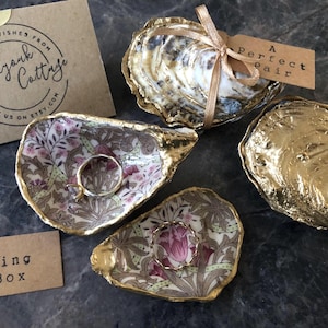 May include: Two oyster shell ring dishes, one with a floral pattern and one with gold paint. A third oyster shell ring dish is shown with a natural finish and a tag that reads "A perfect pair".
