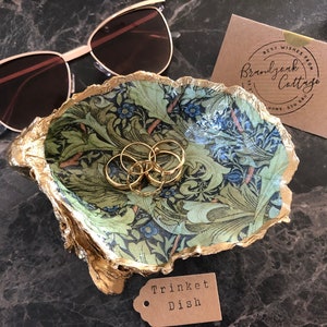 Könnte beinhalten: Eine goldene Schmuckschale mit einem grünen und blauen Blumenmuster. Die Schale steht auf einer schwarzen Oberfläche mit einer Sonnenbrille und einer Karte mit der Aufschrift "Beste Wünsche von Brandywine Cottage".