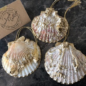 May include: Three white seashell ornaments with gold accents. The shells are decorated with gold paint and have a rustic, vintage look.