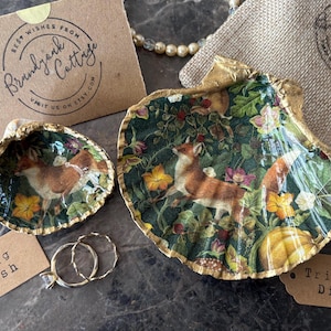 May include: Two decorative shell dishes with gold trim. The larger dish features a green and brown floral pattern with a fox design. The smaller dish features a similar pattern with a fox design. The text "Ring Dish" and "Trinket Dish" are on labels below the dishes.
