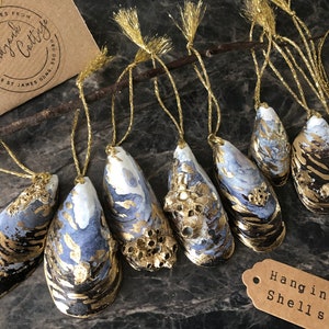 May include: Hand-painted hanging shells with gold accents and blue and white details. Each shell is suspended by a gold string. A small tag reads "Hanging Shells". A card reads "Best Wishes From Brandyjack Cottage".