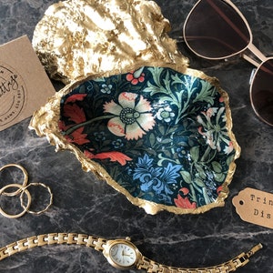 Pu&ograve; includere: Un portagioie decorativo a forma di conchiglia, con un motivo floreale blu, rosso e verde. Il bordo &egrave; dorato. Sono presenti anche anelli d'oro, un orologio d'oro e occhiali da sole.