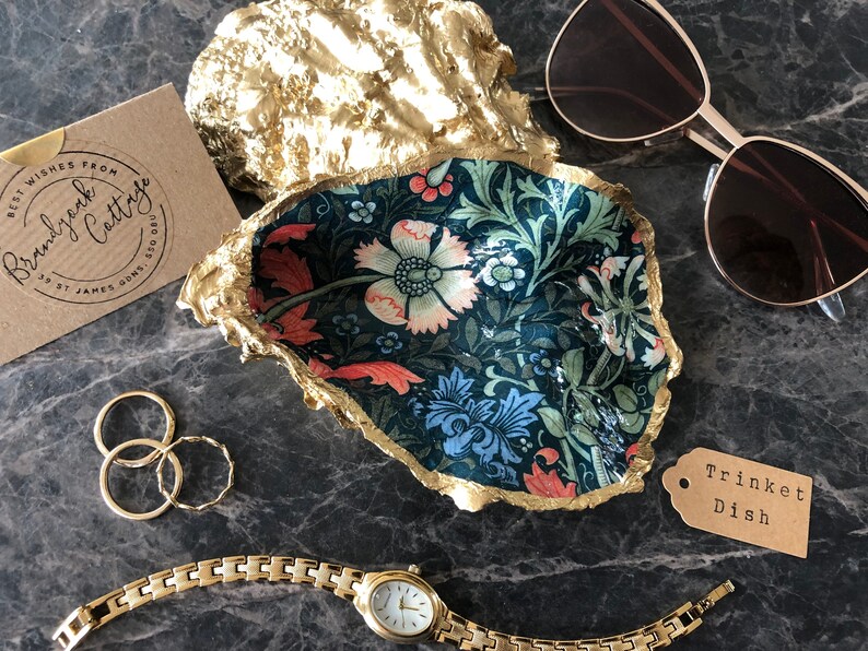 Pu&ograve; includere: Un portagioie decorativo a forma di conchiglia, con un motivo floreale blu, rosso e verde. Il bordo &egrave; dorato. Sono presenti anche anelli d'oro, un orologio d'oro e occhiali da sole.