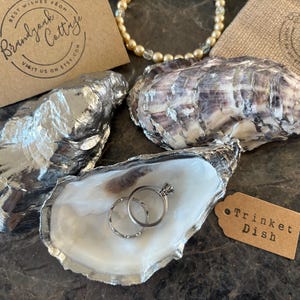 May include: A set of three ceramic mugs with a speckled, cream-colored glaze. Each mug features a different hand-painted design: a blue and green leaf, a yellow flower, and a red berry. The mugs have a simple, modern design.