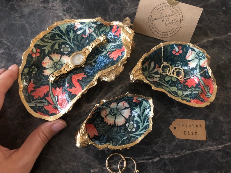 Pu&ograve; includere: Set di tre vassoi decorativi per bigiotteria con motivo floreale nei toni del verde, rosso e crema. I bordi sono rifiniti in oro. Un orologio e una collana d'oro sono esposti. Un'etichetta recita "Trinket Dish".