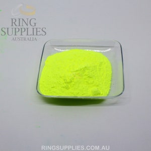 May include: A clear, square glass dish filled with bright neon yellow powder. The powder has a fine, granular texture. The image also includes the text "RING SUPPLIES AUSTRALIA" and "RINGSUPPLIES.COM.AU" in the upper left and lower right corners.