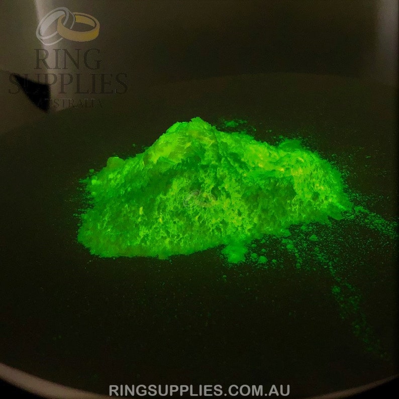 May include: A pile of bright neon green powder sits on a dark surface. The powder glows intensely, creating a striking contrast against the black background. The image includes the text "RING SUPPLIES AUSTRALIA" and "RINGSUPPLIES.COM.AU".