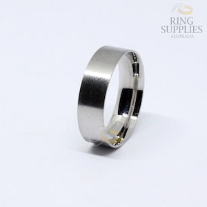 May include: A silver ring blank with a flat top and a rounded edge. The ring is made of metal and is ready to be engraved or set with a stone.