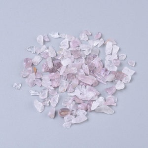 May include: A collection of small, pink and clear quartz crystals. The crystals are scattered on a light grey background.