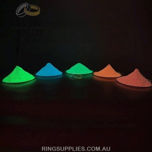 May include: A dark image showcasing four piles of glowing powder in green, blue, green, and orange hues. Each pile sits on a small, round, dark plate. The website address ringsupplies.com.au is visible at the bottom.