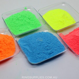 May include: Five small, clear square dishes each filled with a different color of powder. The colors are neon green, neon yellow, neon orange, bright blue, and neon pink. The text "RING SUPPLIES AUSTRALIA" is in the upper left corner.