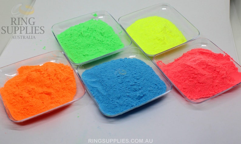 May include: Five small, clear square dishes each filled with a different color of powder. The colors are neon green, neon yellow, neon orange, bright blue, and neon pink. The text "RING SUPPLIES AUSTRALIA" is in the upper left corner.