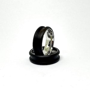 May include: Two black and silver rings stacked on top of each other. The top ring is made of black wood and the bottom ring is made of silver.