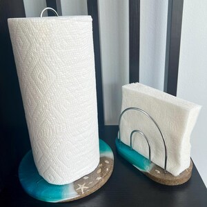 May include: A turquoise and white resin paper towel holder with a silver metal ring and a roll of paper towels. Next to it is a matching turquoise and white resin napkin holder with a silver metal rack.