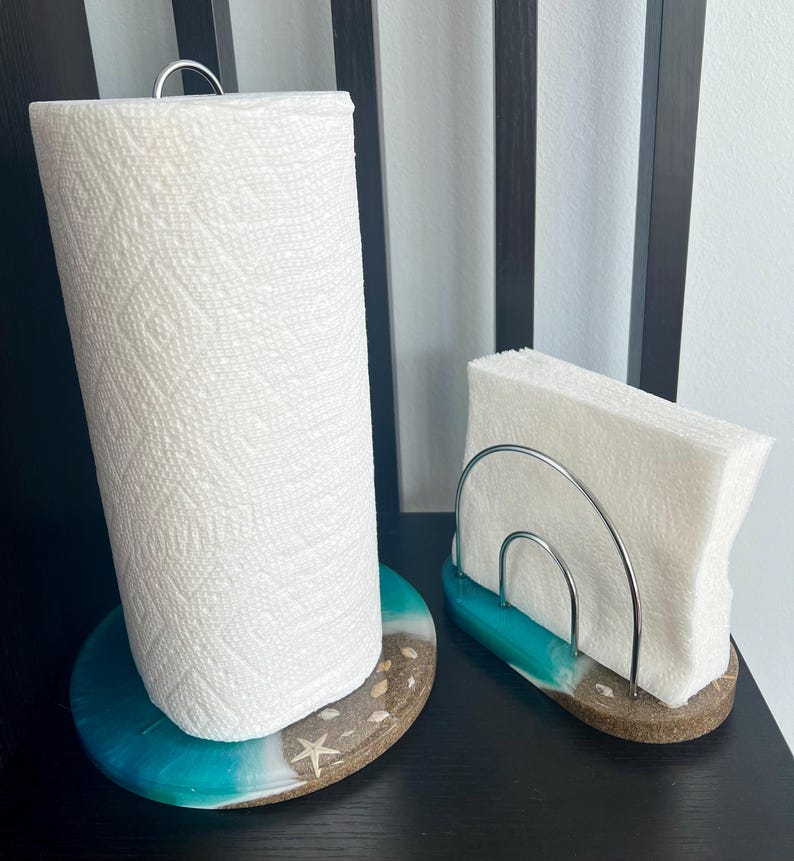 May include: A turquoise and white resin paper towel holder with a silver metal ring and a roll of paper towels. Next to it is a matching turquoise and white resin napkin holder with a silver metal rack.