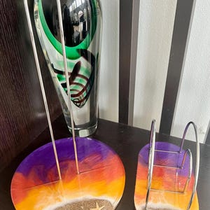 May include: Two resin paper towel holders with a sunset design. The holders are round and have a white sandy beach base with seashells and a starfish. One holder is for paper towels and the other is for napkins.
