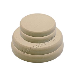 May include: A stack of four unfinished, round wooden coasters. The coasters are varying sizes, with the largest at the bottom and the smallest at the top. The wood has a light tan colour. The text "LaserWorkUK" is visible on the side of the bottom coaster.