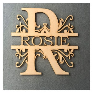 May include: Wooden cutout of the letter R with the name "ROSIE" cut out inside the letter. The letter has a decorative flourish design.