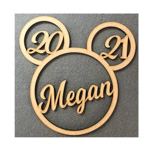 May include: Wooden Mickey Mouse-shaped ornament with the numbers 20 and 21 in the ears and the name Megan in the centre.