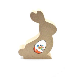 May include: A wooden bunny rabbit shaped Easter egg holder with a cut-out for a Kinder Surprise egg. The bunny is light brown and has a simple design.