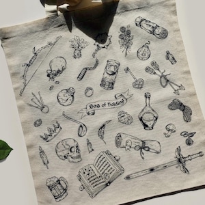 Könnte beinhalten: Eine weiße Canvas-Tragetasche mit einer schwarz-weißen Illustration verschiedener Fantasy-Gegenstände, darunter ein Schwert, eine Krone, eine Zaubertrankflasche, ein Schädel, ein Buch, eine Feder, eine Schriftrolle, ein Schlüssel, Pfeil und Bogen, ein Kelch und ein Beutel zum Aufbewahren. Der Text "Bag of Holding" ist auf der Tasche aufgedruckt.