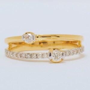Op de afbeelding: Een gouden ring met twee diamanten in de band. De ring is ontworpen met een dubbele band, een met een enkele diamant en de andere met een rij kleinere diamanten.