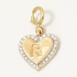 Puede incluir: Un dije dorado en forma de corazón con un borde engastado con diamantes. El dije presenta la letra "R" en el centro. El dije tiene un cierre para una fácil fijación a una pulsera o collar.