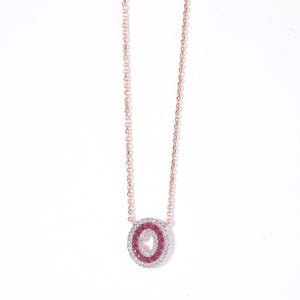 May include: Rose gold necklace with a double oval pendant. The inner oval is filled with pink gemstones, and the outer oval is encrusted with clear gemstones. The chain is delicate and hangs from the pendant.