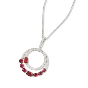 May include: A silver-toned necklace featuring a circular pendant encrusted with small white stones. The pendant is accented with a curved row of seven oval-shaped deep red gemstones of varying sizes along the lower left edge.