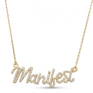 May include: A gold-colored necklace with the word "Manifest" spelled out in cursive. The letters are encrusted with small, sparkling stones. The necklace hangs from a delicate chain.