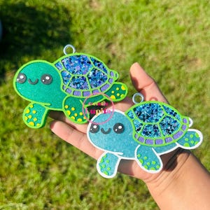 May include: Two green and blue glitter turtle ornaments with smiling faces and green and white polka dots.