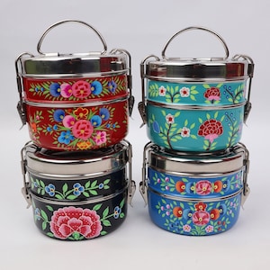 May include: Four stainless steel lunch boxes with painted floral designs. The lunch boxes are stacked in pairs, with red and black on the left and turquoise and blue on the right. Each lunch box has two tiers.