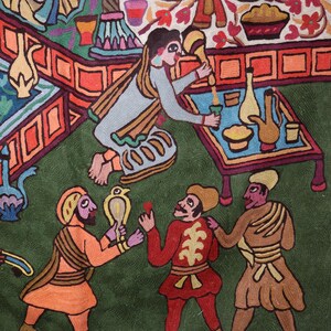 May include: A colorful embroidered artwork depicting a scene with multiple figures. The figures are dressed in various colors and patterns, including red, blue, green, and yellow. The artwork is set against a green background and features a table with a variety of objects, including a pitcher, a bowl, and a plate.