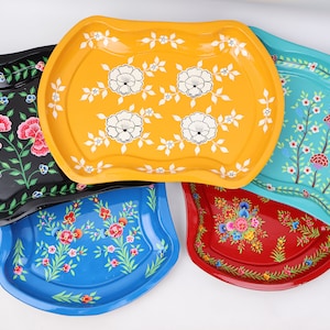 Puede incluir: Cinco bandejas decorativas con diseños florales. Las bandejas son de metal y tienen un borde festoneado. Las bandejas están pintadas en varios colores, incluyendo negro, amarillo, azul, turquesa y rojo.