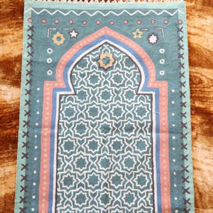 May include: A teal blue prayer rug with a geometric pattern and a traditional arch design. The rug has pink, yellow, and blue borders.
