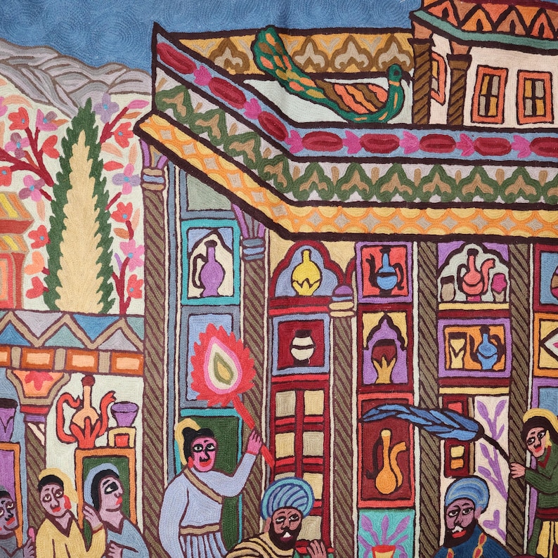 May include: A colorful embroidered tapestry depicting a scene with a peacock on a rooftop, people in traditional clothing, and a building with intricate details. The tapestry is made with wool and features a variety of colors, including red, blue, green, yellow, and orange.
