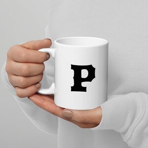 Può includere: Tazza in ceramica bianca con la lettera "P" nera. La tazza ha un manico e una superficie lucida. Un design classico per gustare tè, caffè o qualsiasi bevanda preferita.