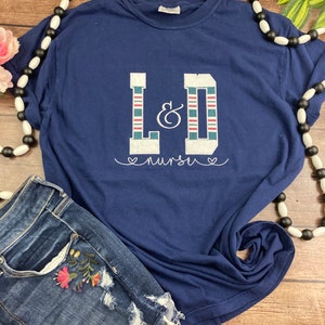 May include: A navy blue t-shirt with a white, red, and green striped L&D graphic and the text "nurse" in white with hearts on either side.