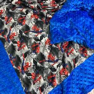 May include: A blue weighted blanket with a Spiderman print on one side. The blanket is made of soft, plush fabric and has a quilted design.