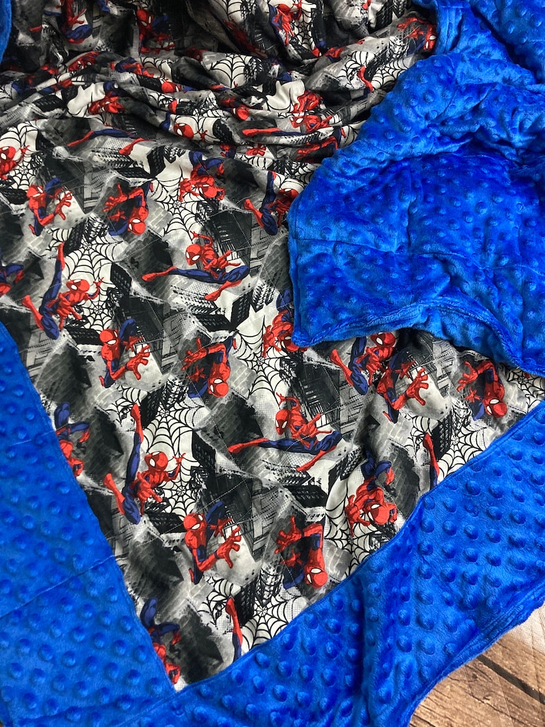 May include: A blue weighted blanket with a Spiderman print on one side. The blanket is made of soft, plush fabric and has a quilted design.