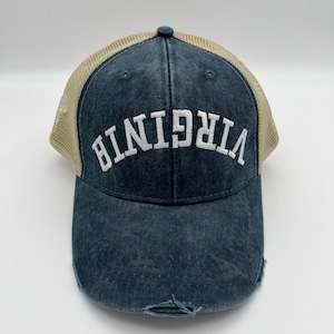 May include: A blue and beige trucker hat with the word "VIRGINIA" embroidered in white on the front. The hat has a distressed look with a frayed brim.