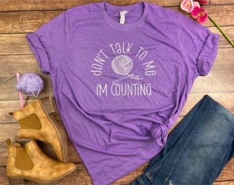 May include: Purple t-shirt with the text "Don't talk to me I'm counting" and a white illustration of yarn and knitting needles.
