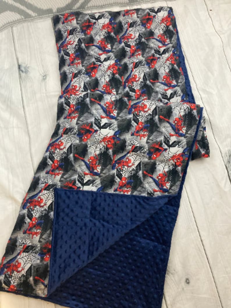 May include: A blue and white reversible blanket with a Spiderman pattern on one side and a soft, blue minky fabric on the other side.