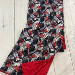 May include: A red and gray baby blanket with a Spiderman print on one side and a red minky fabric on the other side.