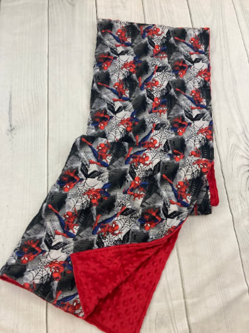 May include: A red and gray baby blanket with a Spiderman print on one side and a red minky fabric on the other side.